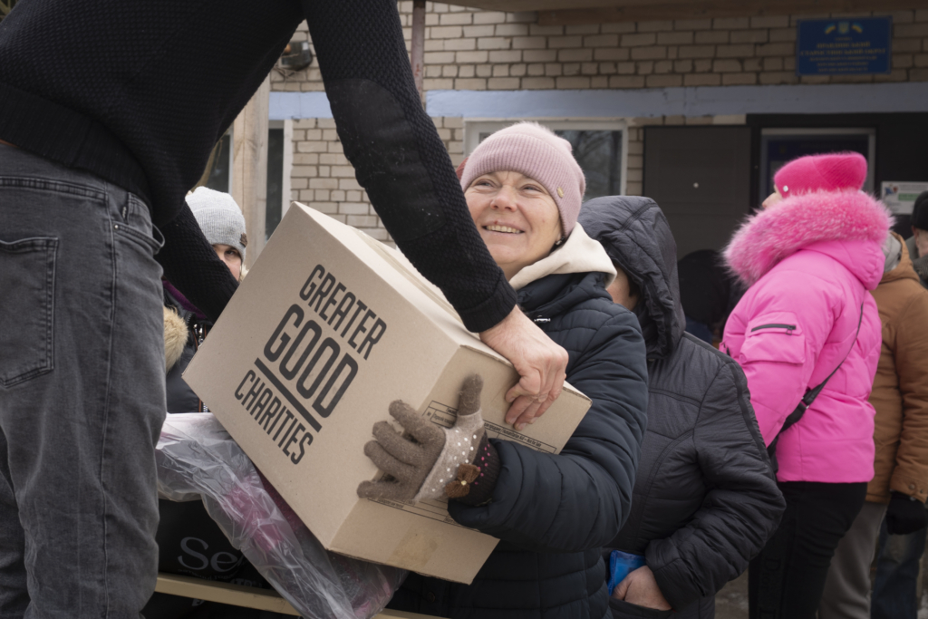 Greater Good Charities employee handing a box to a ukraine woman during a disaster relief distribution